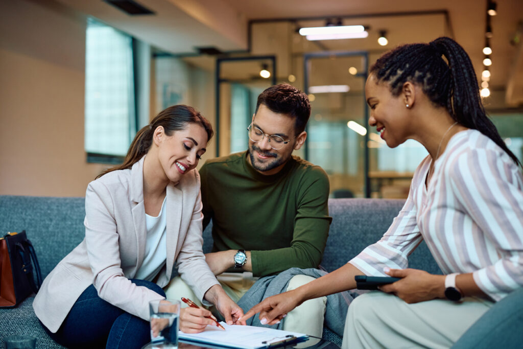 Happy woman signing a contract while being with her husband on a meeting with a mortgage broker